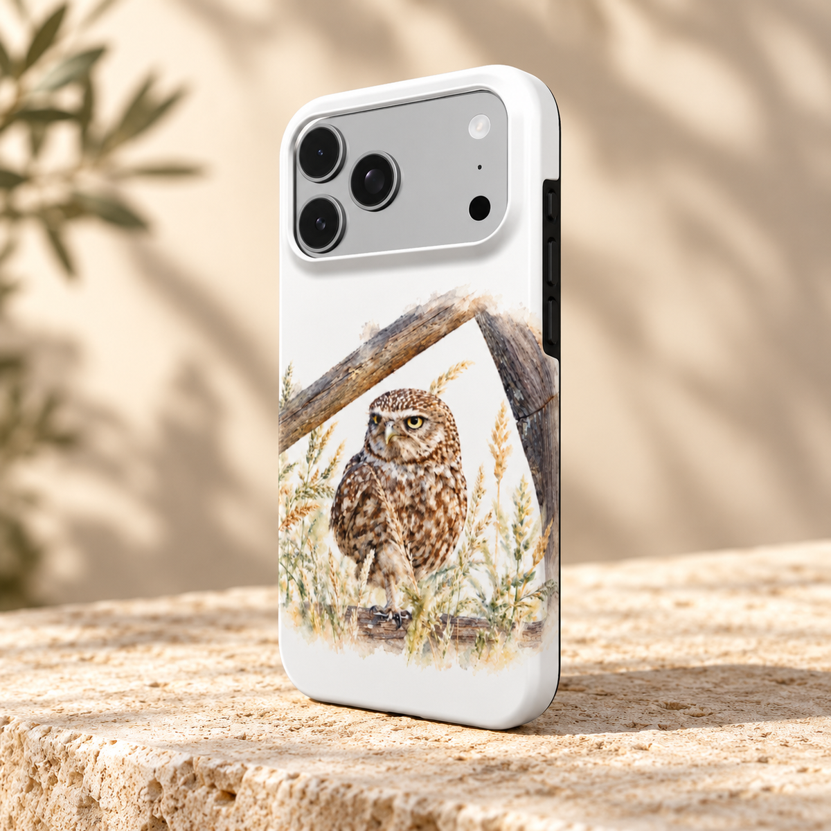 Wit iPhone-hoesje met Steenuil in aquarelstijl, schuin van achteren op een lichte stenen ondergrond.